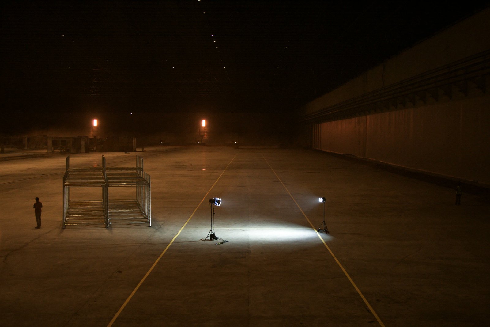 A warehouse aisle at night with the taped lanes lit and the rest of the building dark.